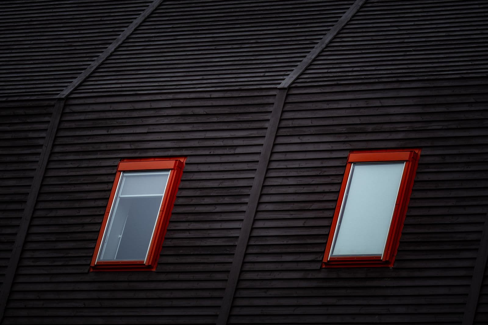 Close-up of a dark wooden roof featuring two red-framed windows adding a modern flair.
